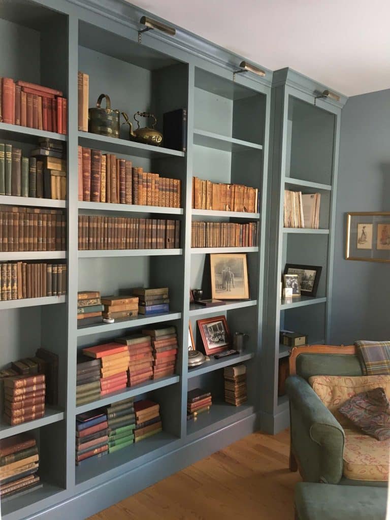 Light green bookcases with rows of books and pictures on them in a home with hardwood floors
