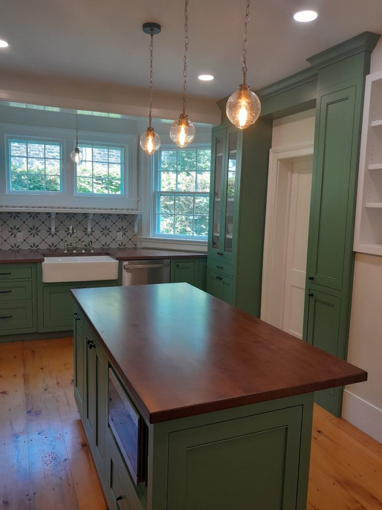 Kitchen area with light green fixtures including green walls, green island with wood top, and hanging light fixtures.